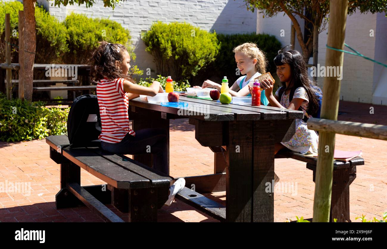 Trois enfants profitent d'un déjeuner ensoleillé en plein air à une table en bois à l'école Banque D'Images