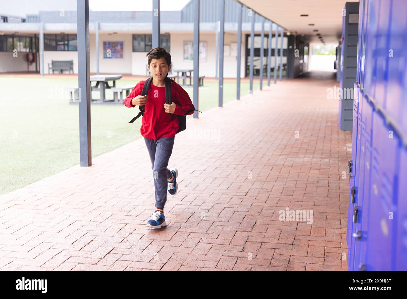 À l'école, un jeune étudiant biracial court dans des casiers à l'extérieur Banque D'Images