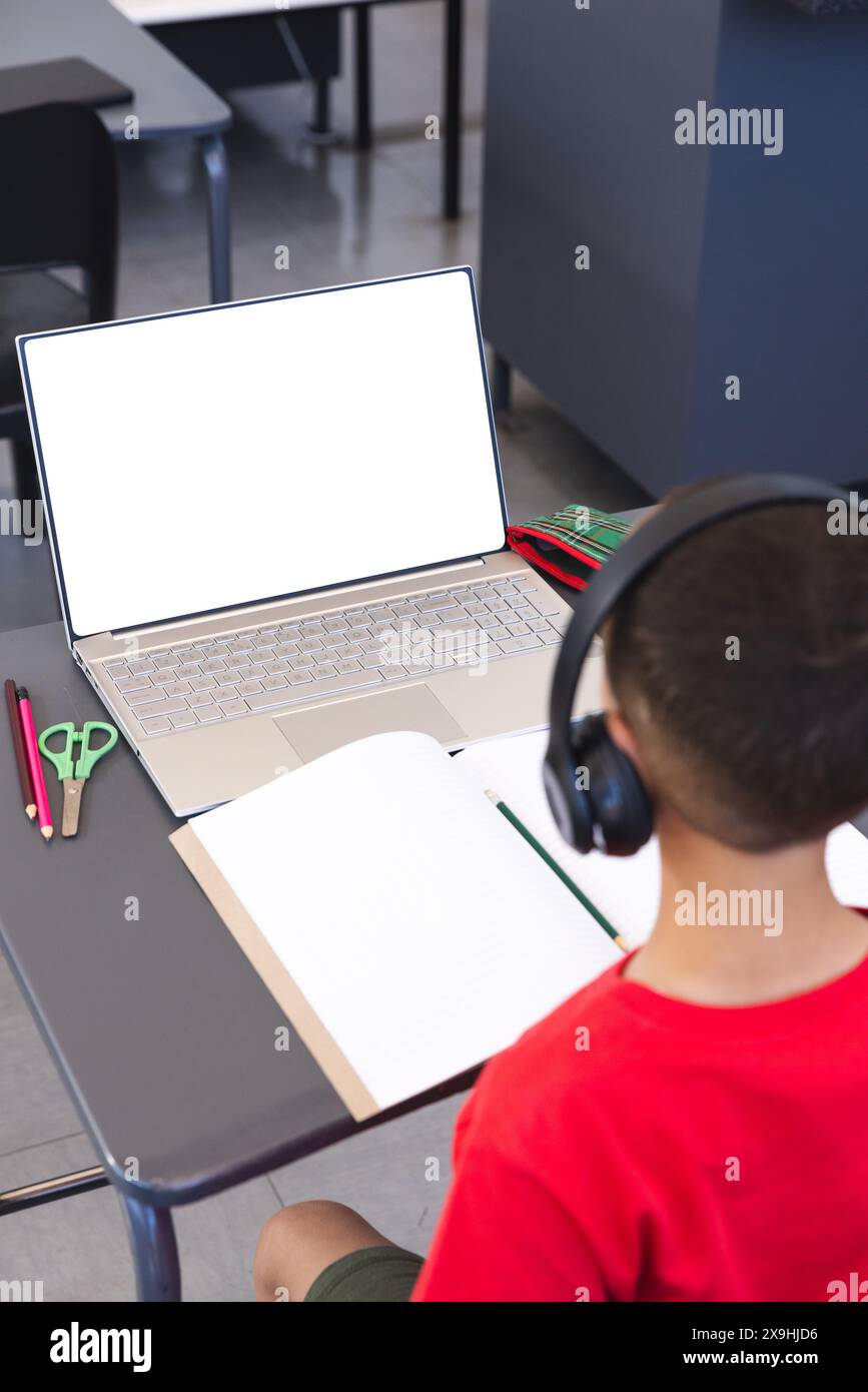 Garçon biracial étudiant à l'école à l'aide d'un ordinateur portable, avec espace de copie Banque D'Images