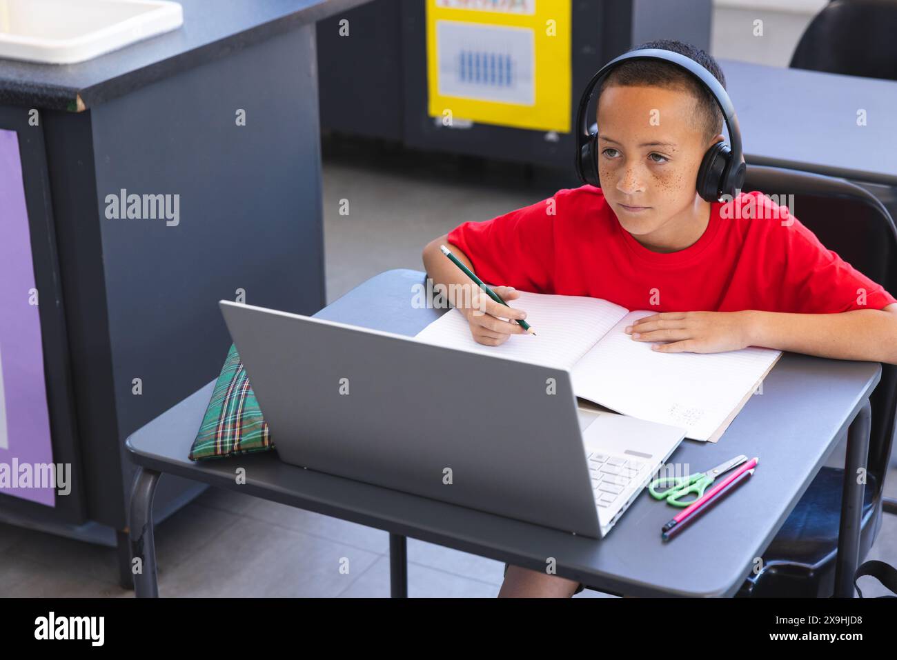 Biracial Boy étudie intentionnellement dans une salle de classe d'école à l'aide d'un ordinateur portable, avec un espace de copie Banque D'Images