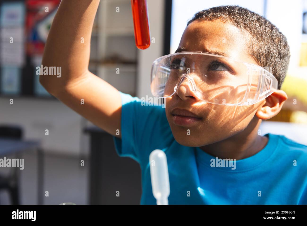 Biracial Boy examine un tube à essai dans un laboratoire de science scolaire Banque D'Images