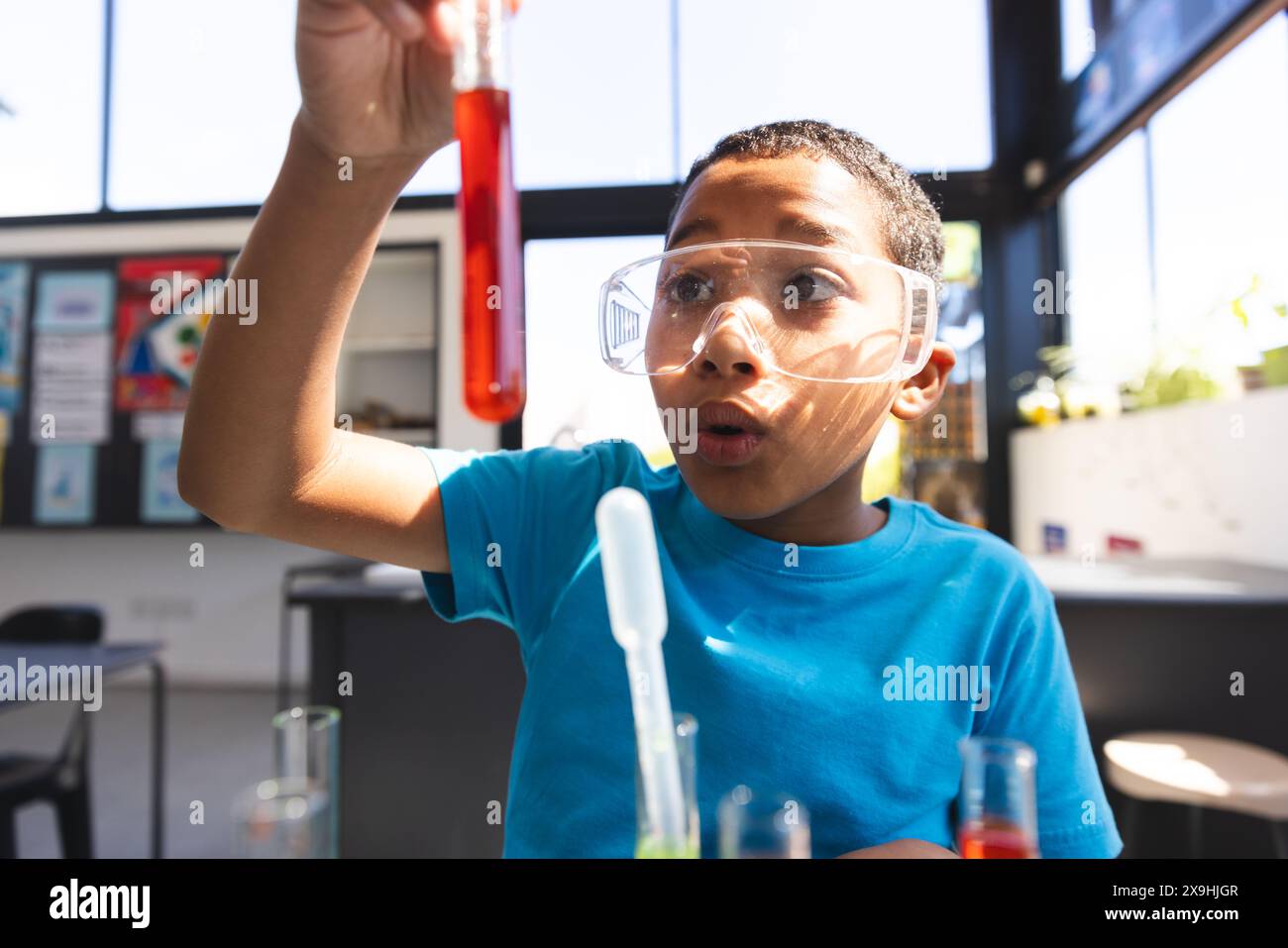 Biracial Boy examine un tube à essai dans un laboratoire de science scolaire Banque D'Images