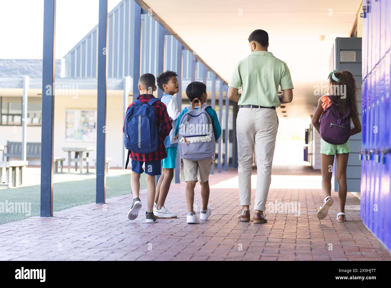 Un jeune homme asiatique, enseignant, conduit trois enfants biraciaux à travers un couloir scolaire Banque D'Images