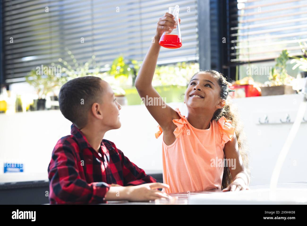 À l'école, fille et garçon biraciaux regardent le liquide rouge dans le flacon, faisant une expérience scientifique Banque D'Images