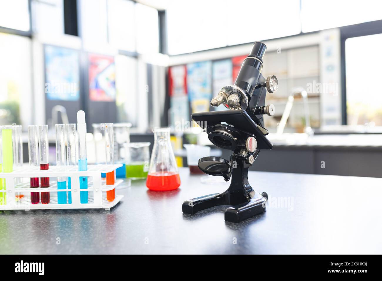 Un microscope est assis sur une table entourée de tubes à essai colorés et de béchers à l'école Banque D'Images