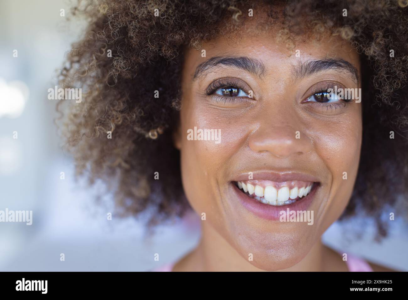 À la maison, jeune femme biraciale portant un haut rose, montrant une expression joyeuse Banque D'Images