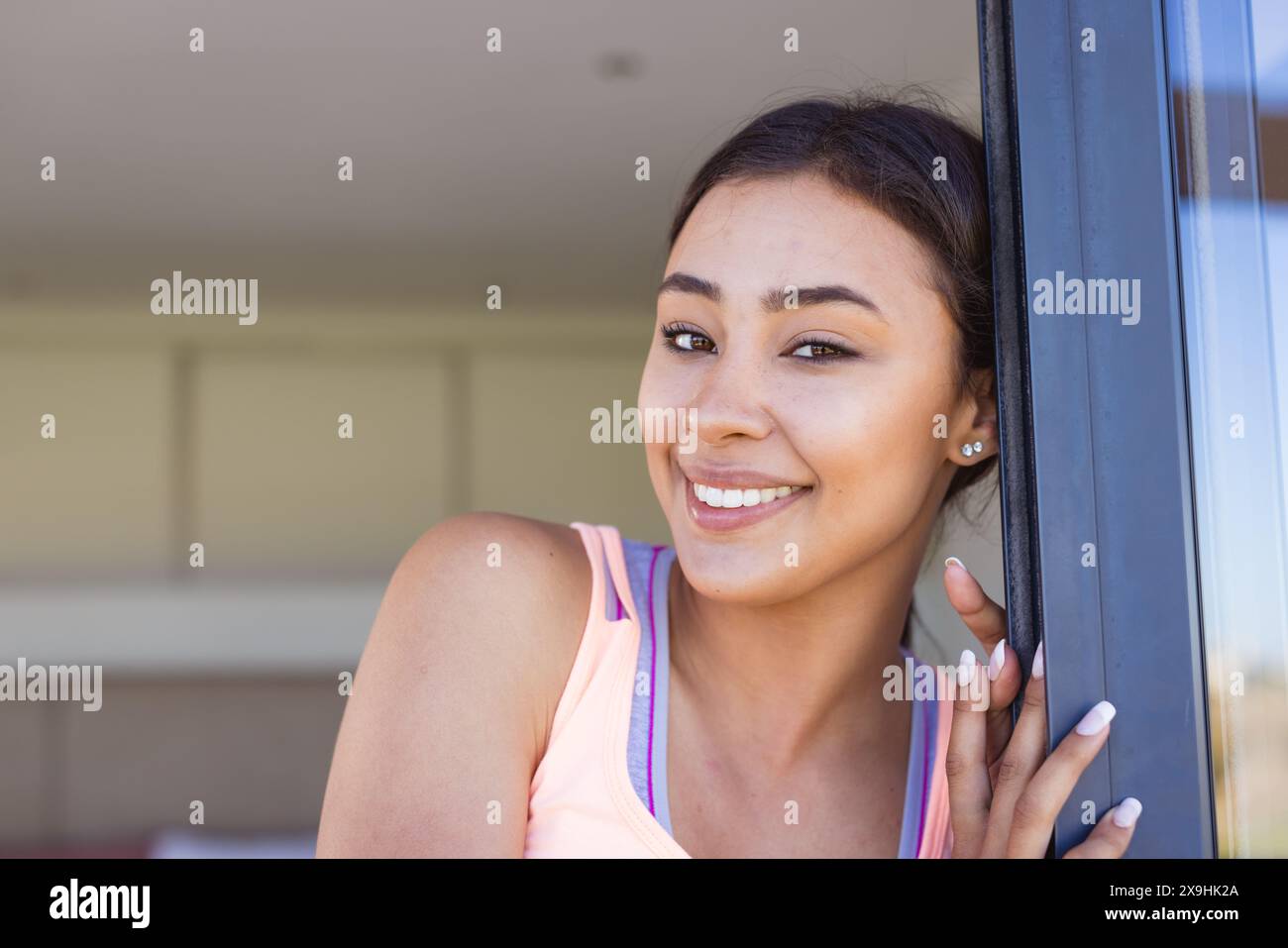 À la maison, jeune femme biraciale appuyée contre une porte, souriant à la caméra Banque D'Images