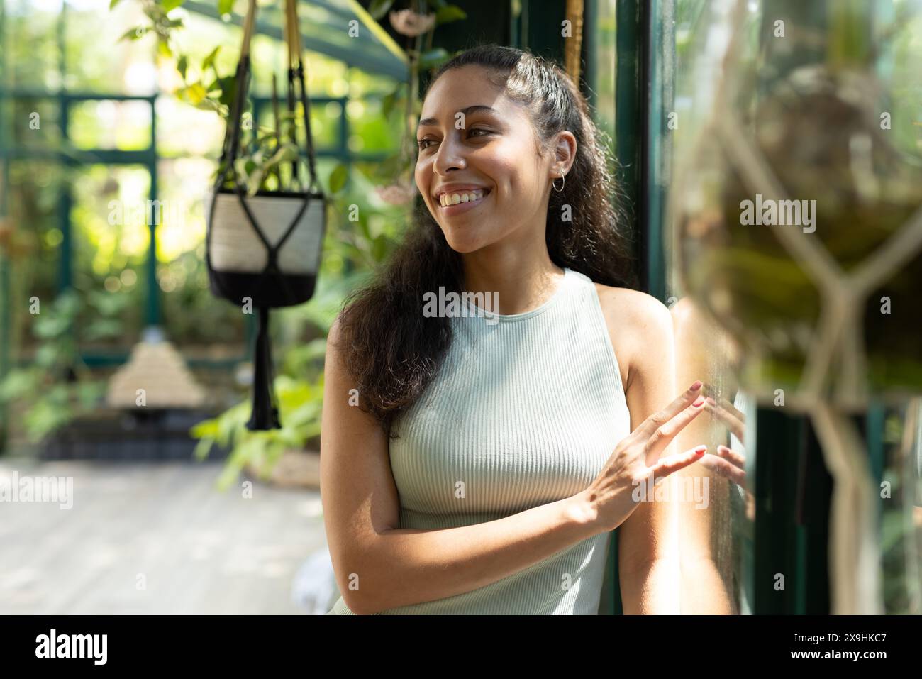 Femme biraciale sourit dans la serre luxuriante de Glass House Studio pendant qu'elle pratique le yoga Banque D'Images