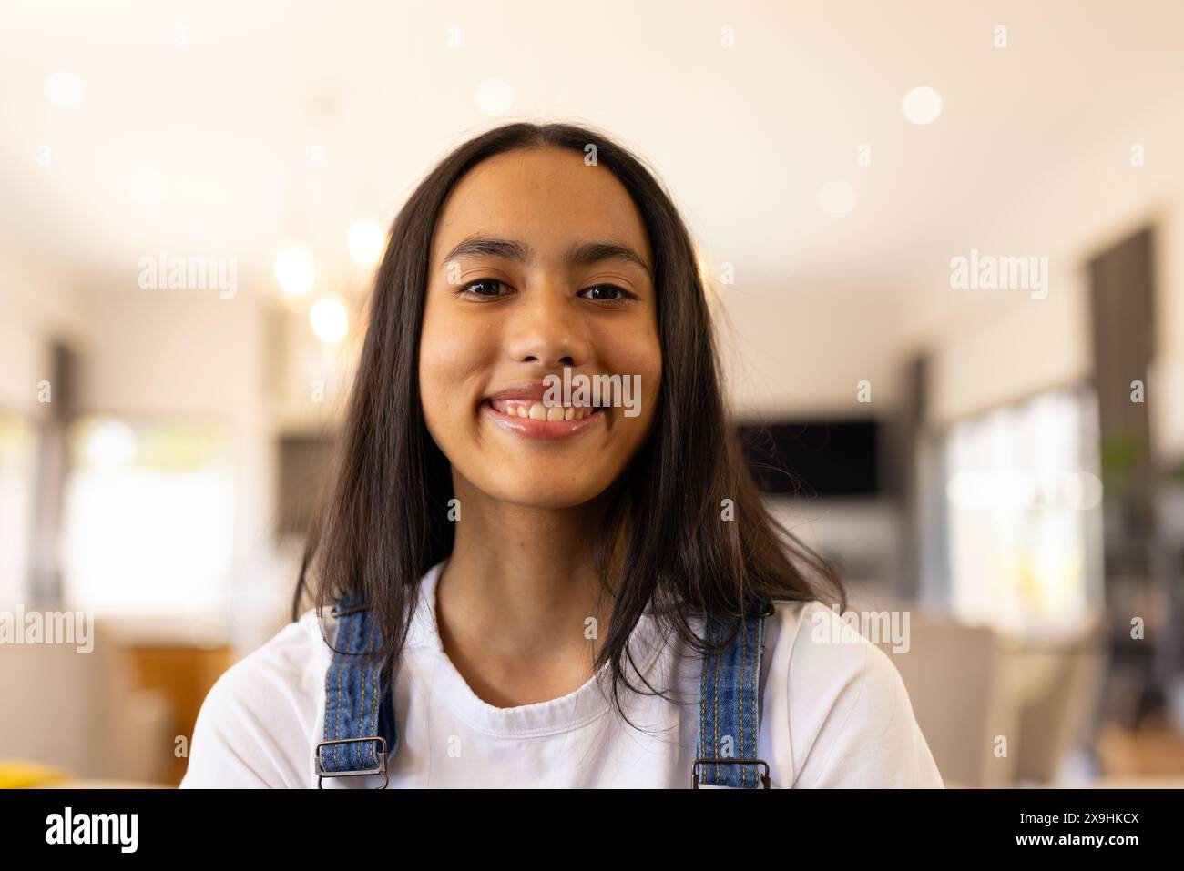 Une jeune fille biraciale portant une salopette en denim, souriant à la maison Banque D'Images