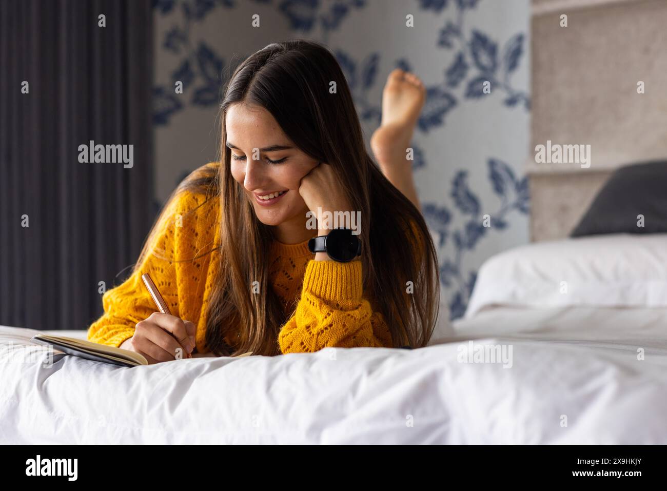 À la maison, jeune femme caucasienne se relaxant et écrivant dans le journal tout en étant allongée sur le lit Banque D'Images