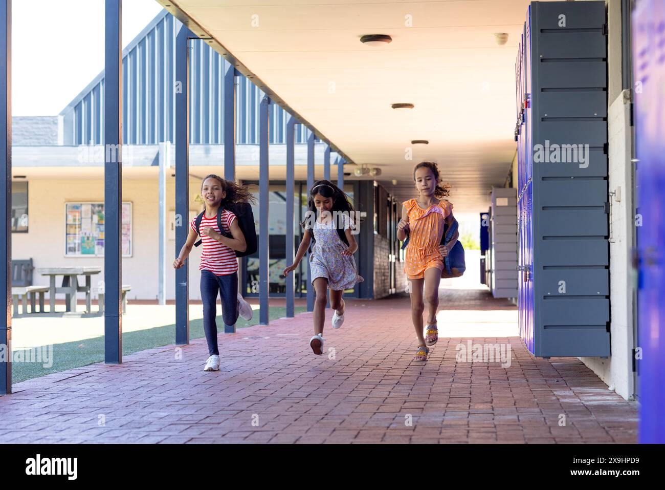 Trois filles biraciales courent joyeusement dans un couloir scolaire Banque D'Images