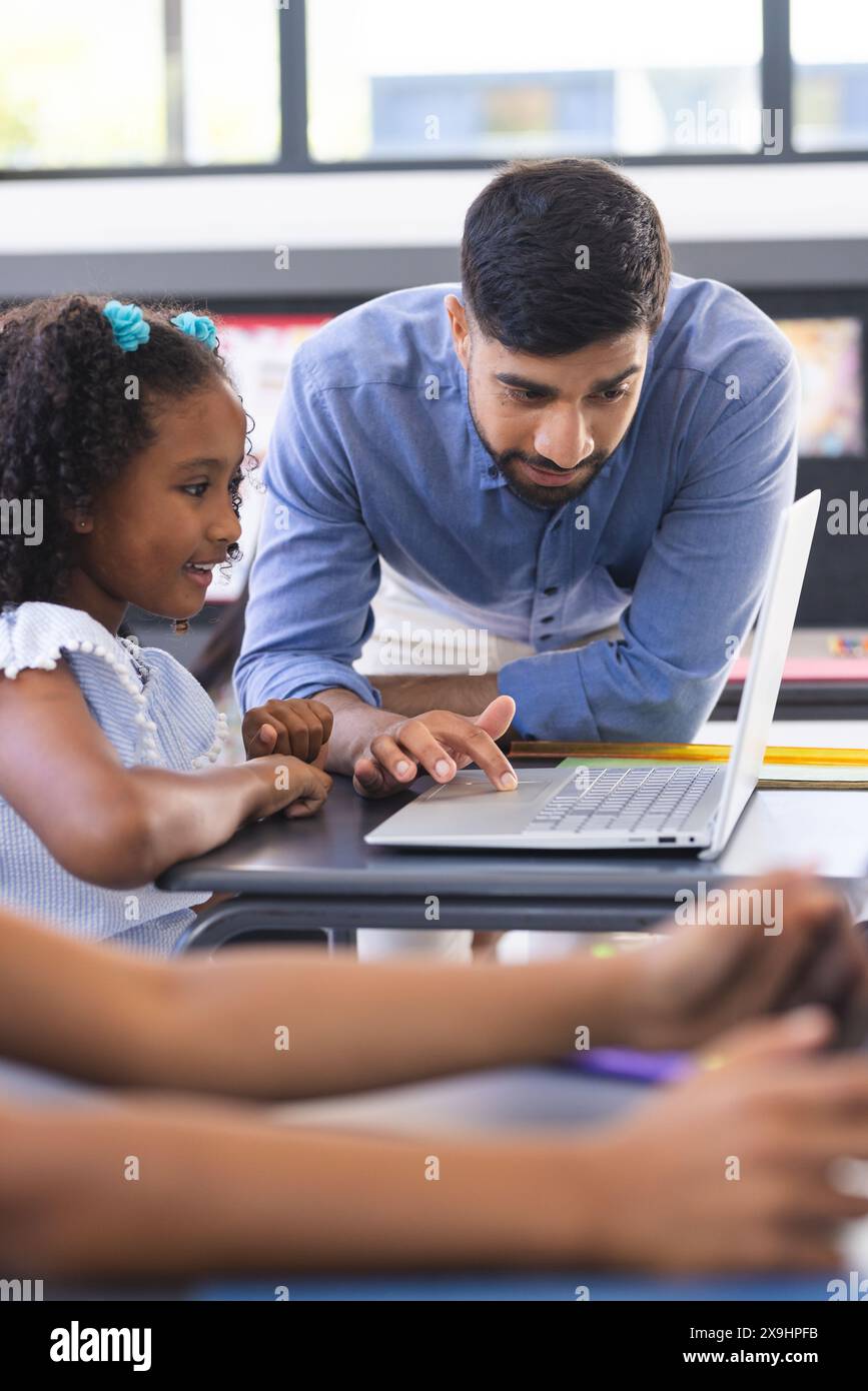 À l'école, enseignant asiatique montrant un ordinateur portable à une étudiante biraciale en classe Banque D'Images