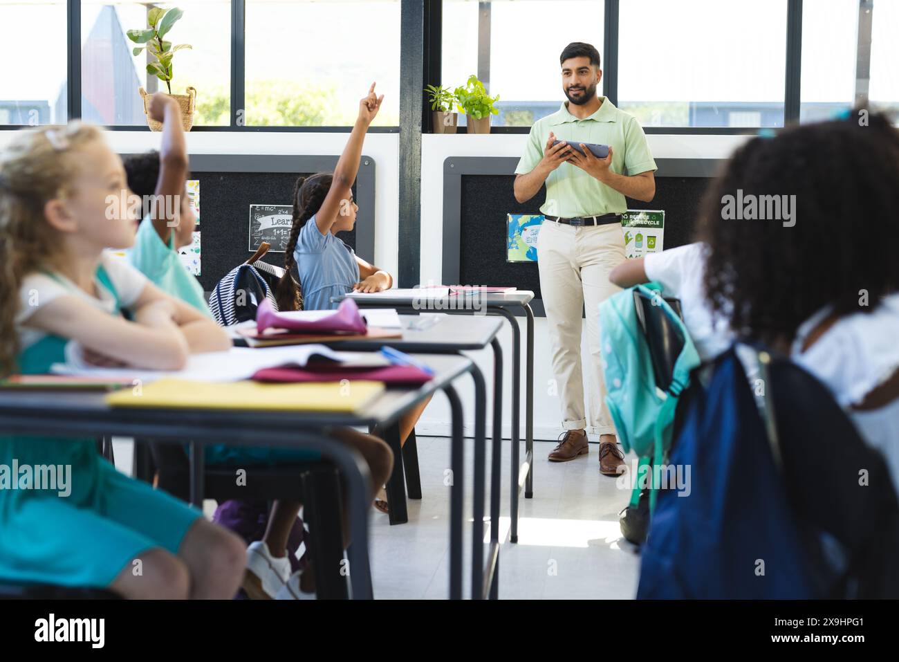 À l'école, les jeunes élèves lèvent la main, l'enseignant asiatique debout Banque D'Images