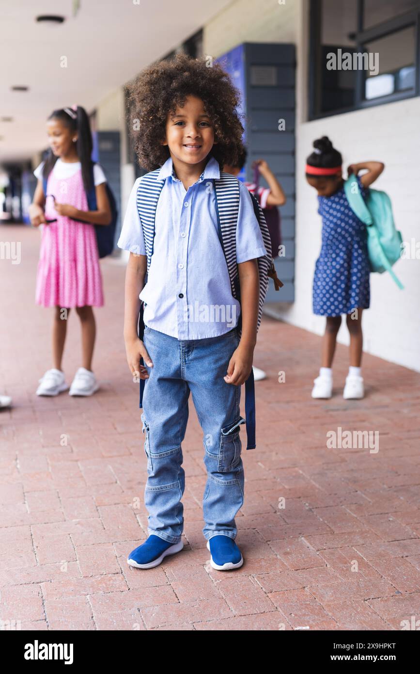 À l'école, un jeune garçon afro-américain se tient souriant avec un sac à dos à l'extérieur Banque D'Images