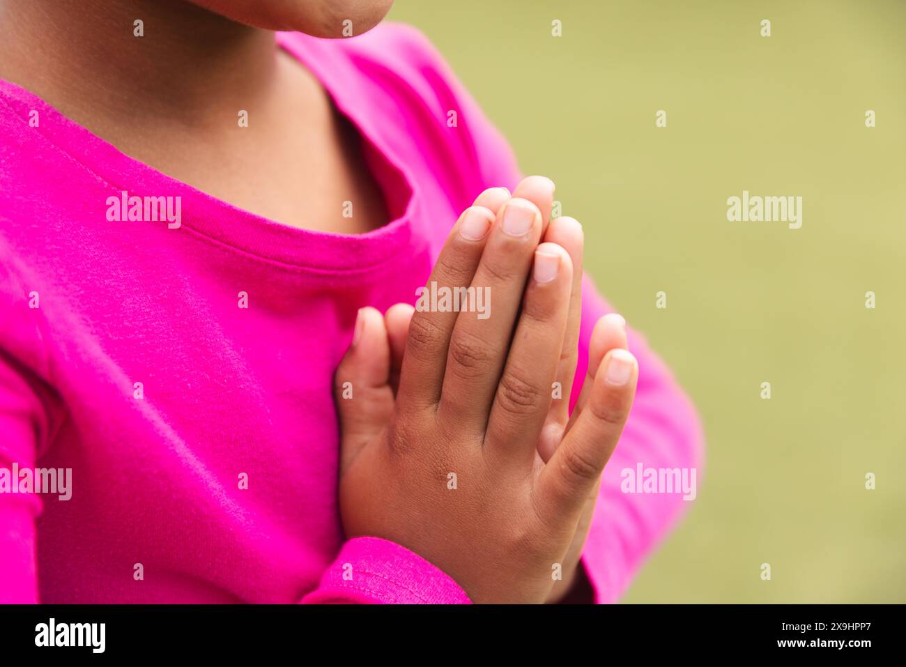 À l'école, une jeune fille biraciale dans un haut rose vif prie à l'extérieur et fait du yoga Banque D'Images