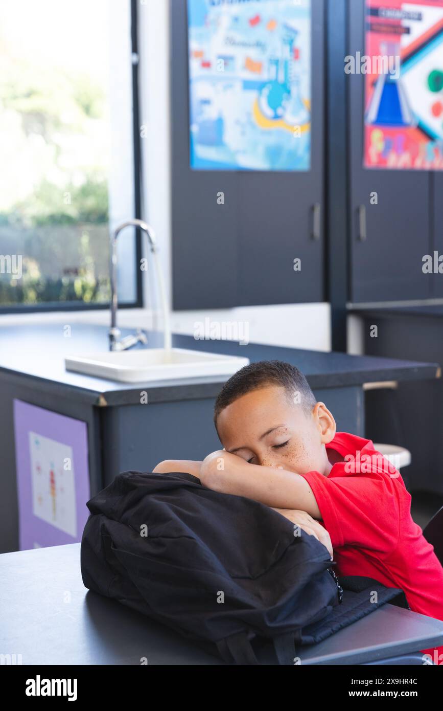 Garçon biracial repose sa tête sur un sac à dos à l'école Banque D'Images