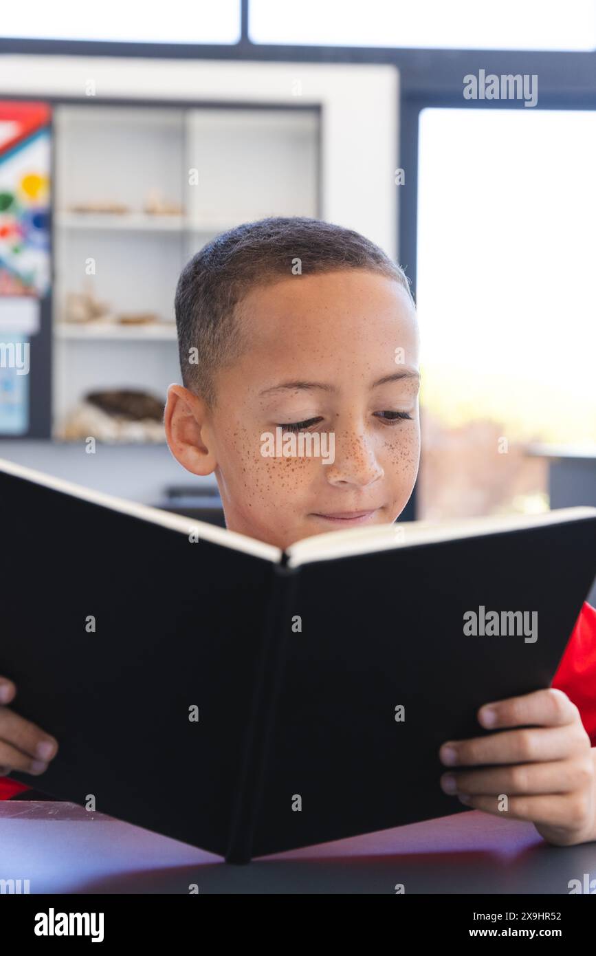 Garçon biracial englouti dans la lecture d'un livre à l'école Banque D'Images