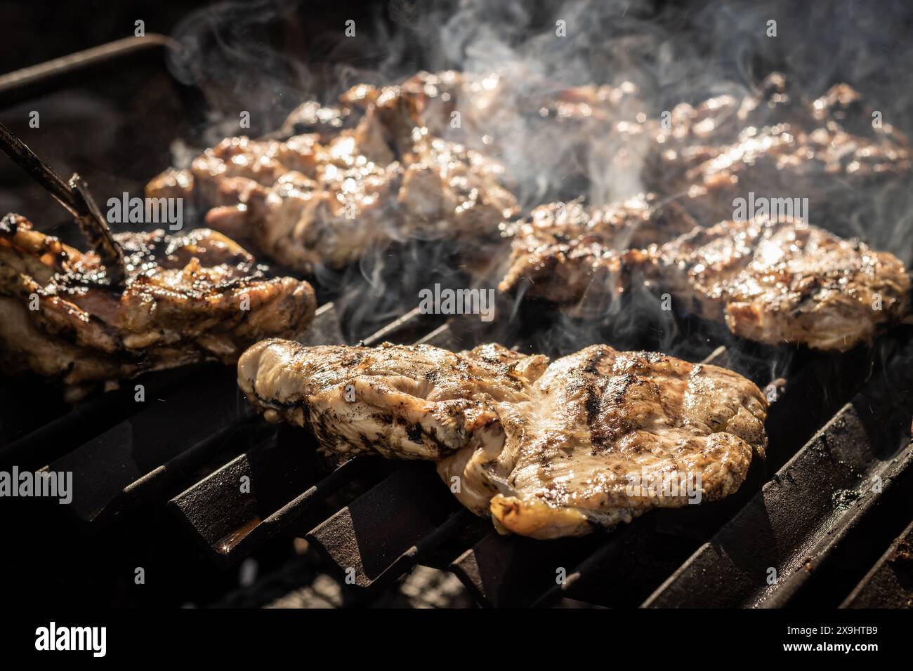 Angle élevé de morceaux de viande appétissants et délicieux avec des fumées placées sur le barbecue dans la cuisine sombre du restaurant à la lumière du jour Banque D'Images