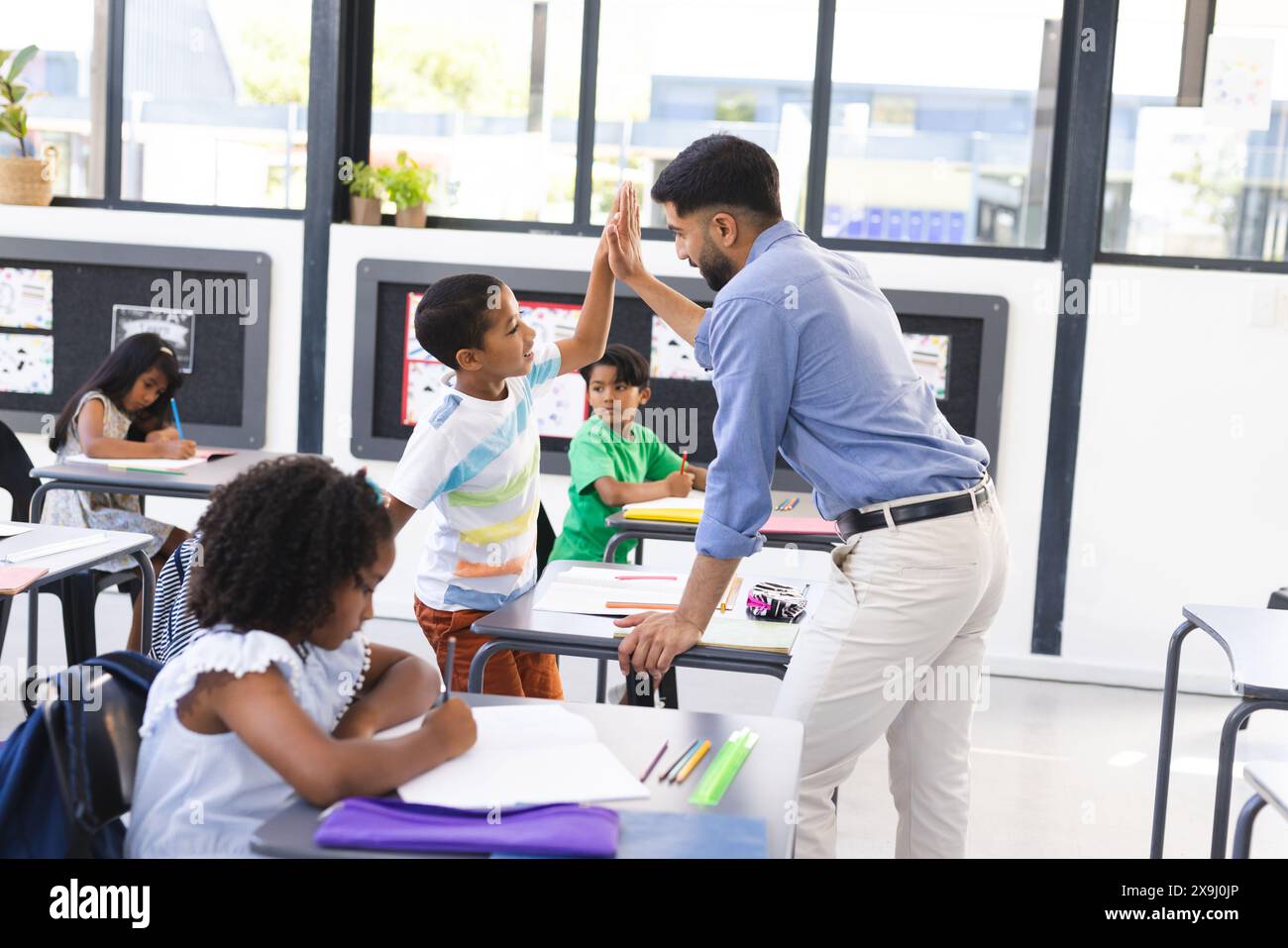 À l'école, jeune enseignant asiatique donnant high-cinq à un élève biracial dans la classe Banque D'Images
