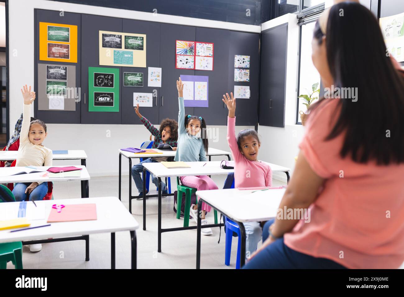 À l'école, les élèves assis à des bureaux levant la main, le professeur face à eux en classe Banque D'Images