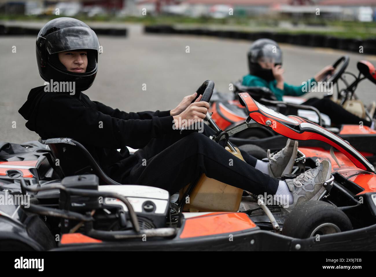 Deux enfants en casques qui font des courses de karts sur une piste en plein air, expérimentant plaisir et excitation. Banque D'Images