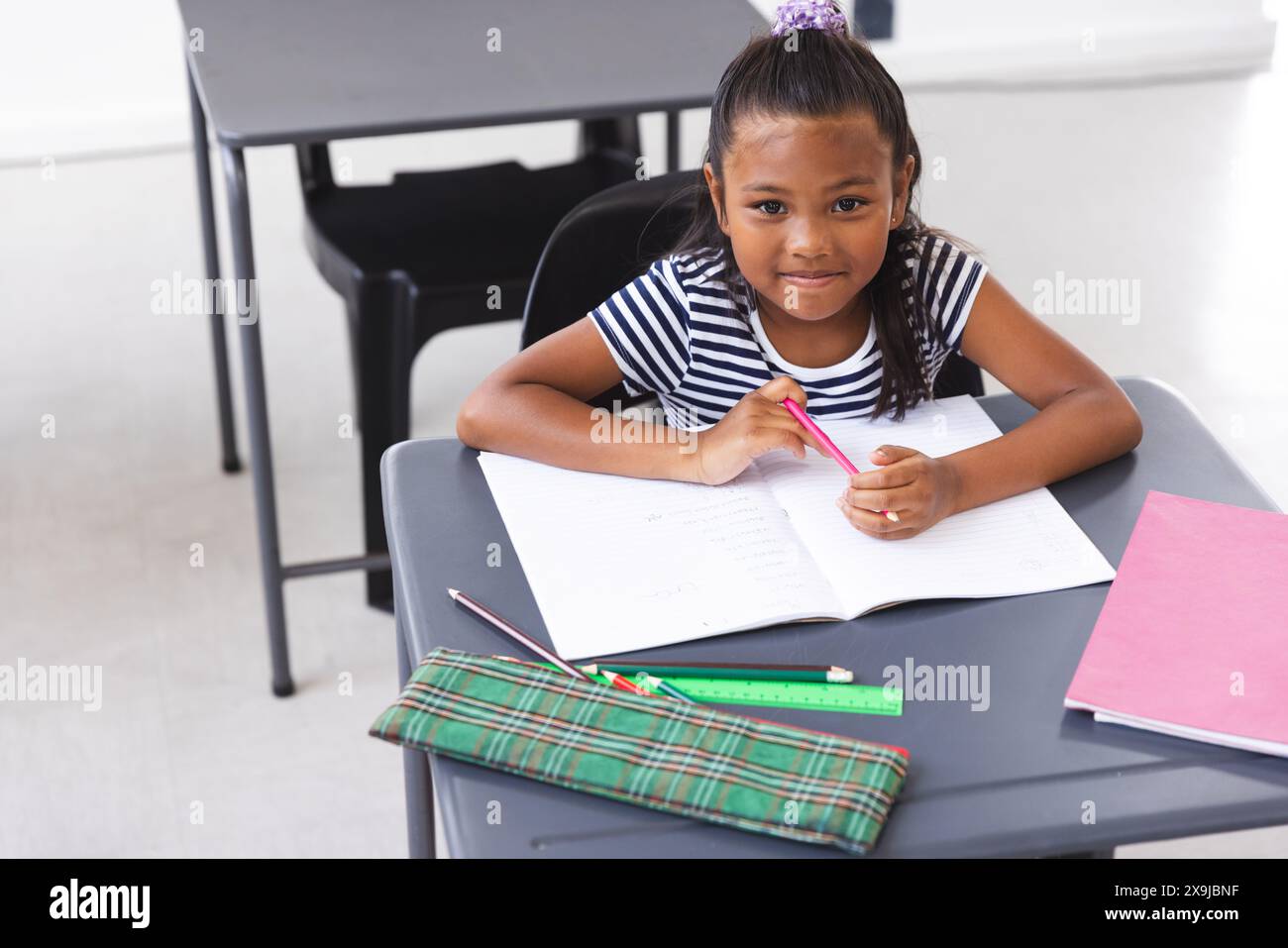 À l'école, jeune fille biraciale assise à un bureau écrivant en classe Banque D'Images