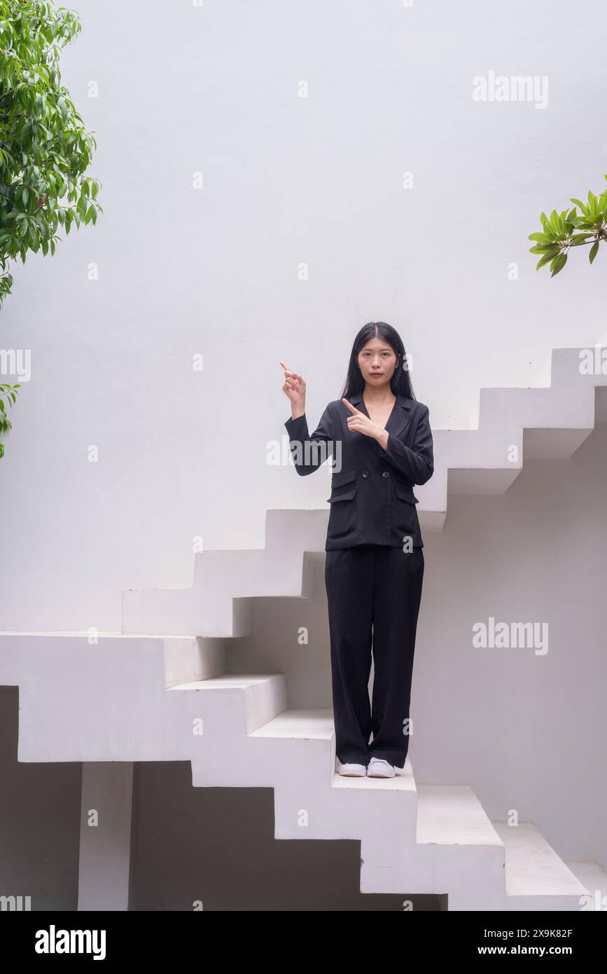 Portrait complet du corps d'une femme professionnelle en tenue d'affaires exsudant la confiance sur les étapes architecturales modernes, y compris la verdure geste avec finge Banque D'Images