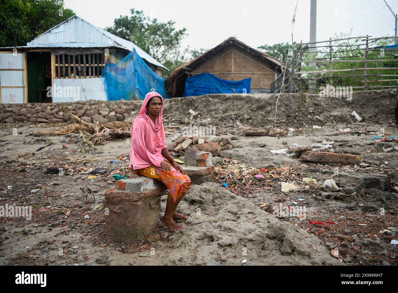 Une femme s'assoit sur les ruines de la maison endommagée au lendemain de la catastrophe à Mongla. Le cyclone Remal, qui a pris naissance dans la baie du Bengale, a frappé les districts côtiers du sud du Bangladesh dans la nuit du dimanche 26 mai. Le cyclone a entraîné des vents dévastateurs de 90 à 120 km/h, entraînant des inondations et des destructions considérables. Les Sundarbans, barrière naturelle critique et site du patrimoine mondial de l'UNESCO, ont subi le plus gros des conséquences du cyclone. Les eaux de crue ont grimpé de trois à quatre pieds au-dessus de la normale, submergeant de vastes zones et causant des dommages importants à la faune et aux infrastructures, y compris Banque D'Images