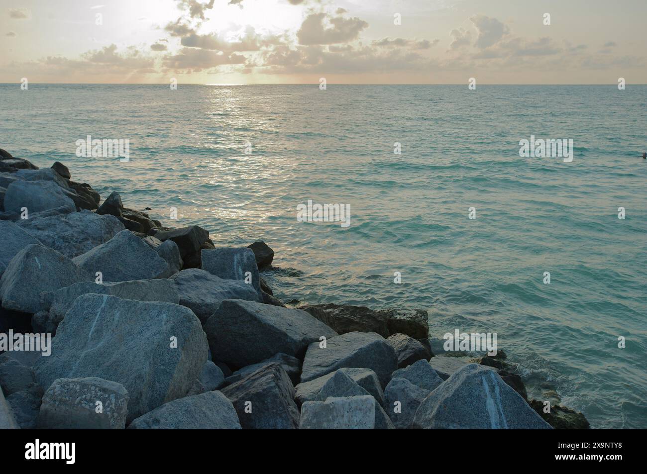 Vue moyenne grands rochers sur le bord du rivage de l'eau près du coucher du soleil en Floride. Multi couleurs et vagues roulant à environ 45 degrés. Pare-soleil Banque D'Images