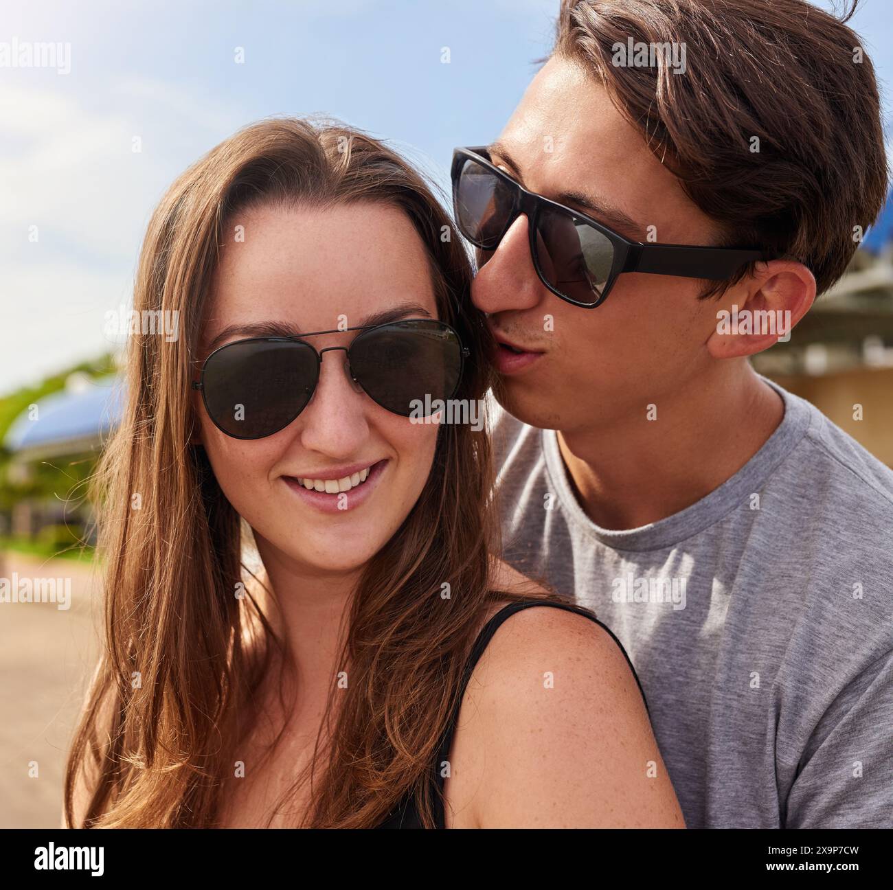 Heureux, en couple ou en plein air pour la relation avec des lunettes de soleil, vacances au soleil ou baiser. Homme, nature ou chuchoter dans l'oreille des femmes pour message secret Banque D'Images