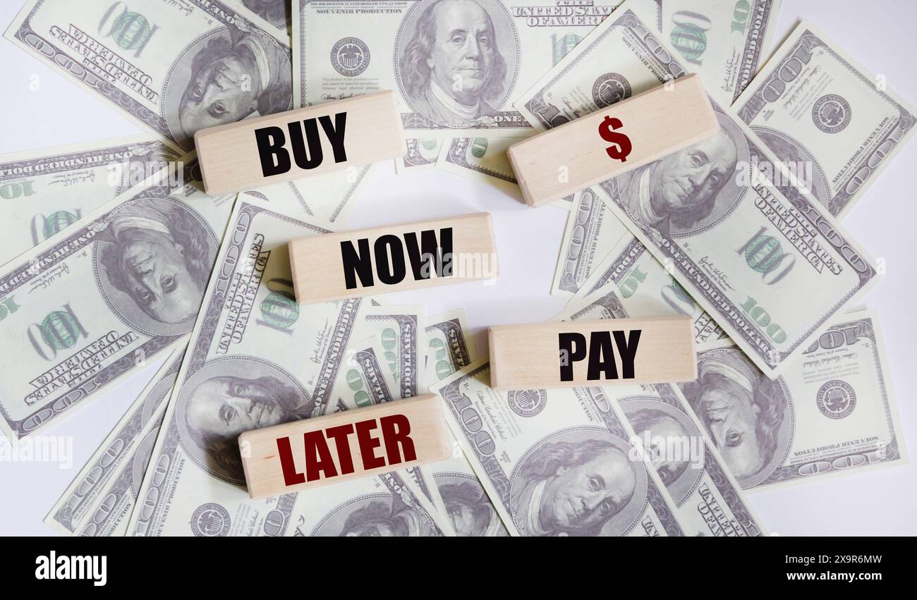 Sur une table blanche, il y a des centaines de billets de dollar et des blocs de bois avec l'inscription ACHETER MAINTENANT - PAYER PLUS TARD Banque D'Images