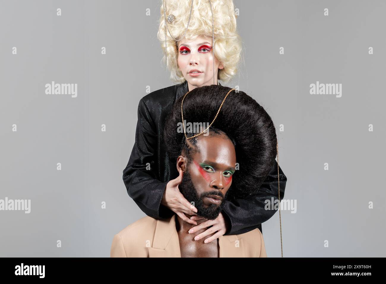 Homme et femme gays confiants, dans des perruques royales vintage et un maquillage audacieux, posant pour un portrait de studio, regardant directement la caméra. Deux amis LGBT en studio photographiés sur fond clair. Banque D'Images