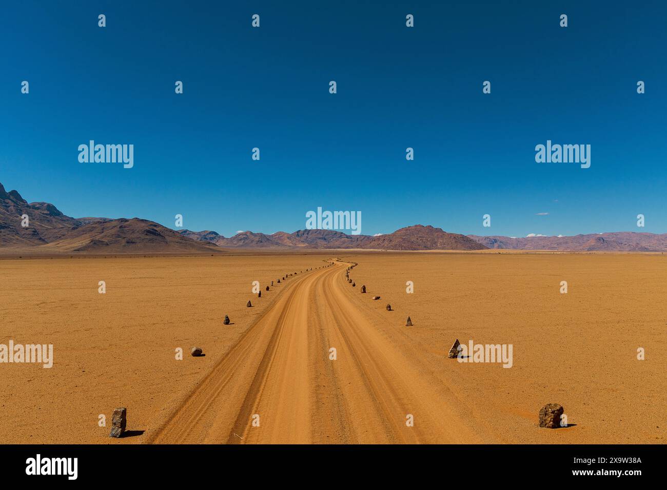 Une route isolée serpente à travers le vaste désert de Namib Naukluft, avec des montagnes majestueuses qui s'élèvent à l'horizon Banque D'Images