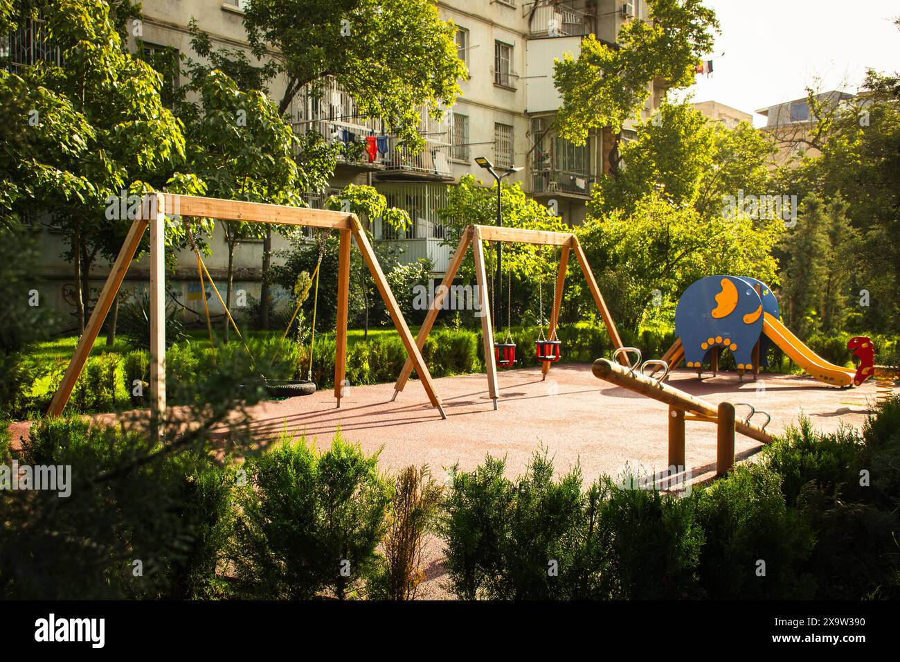 Tbilissi, Géorgie - 1er juin 2024 : Nouveau parc vert avec aire de jeux pour enfants et balançoires par un ancien bâtiment de type soviétique dans la capitale de la région de Saburtalo en Géorgie Banque D'Images