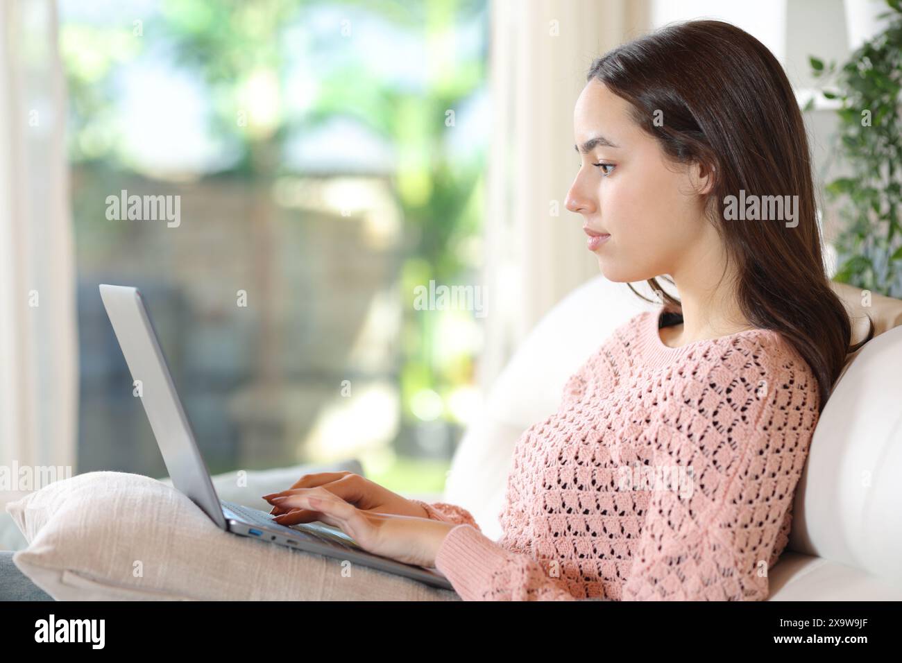 Profil d'une femme sérieuse utilisant un ordinateur portable assis sur un canapé à la maison Banque D'Images