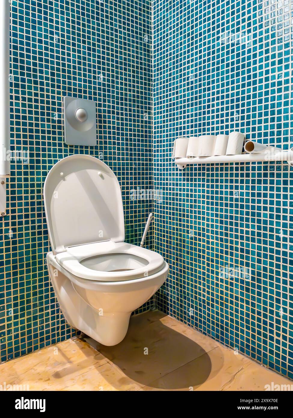 La salle de bains moderne comprend des toilettes murales avec des murs en mosaïque bleue et une étagère contenant des rouleaux de papier hygiénique. Banque D'Images