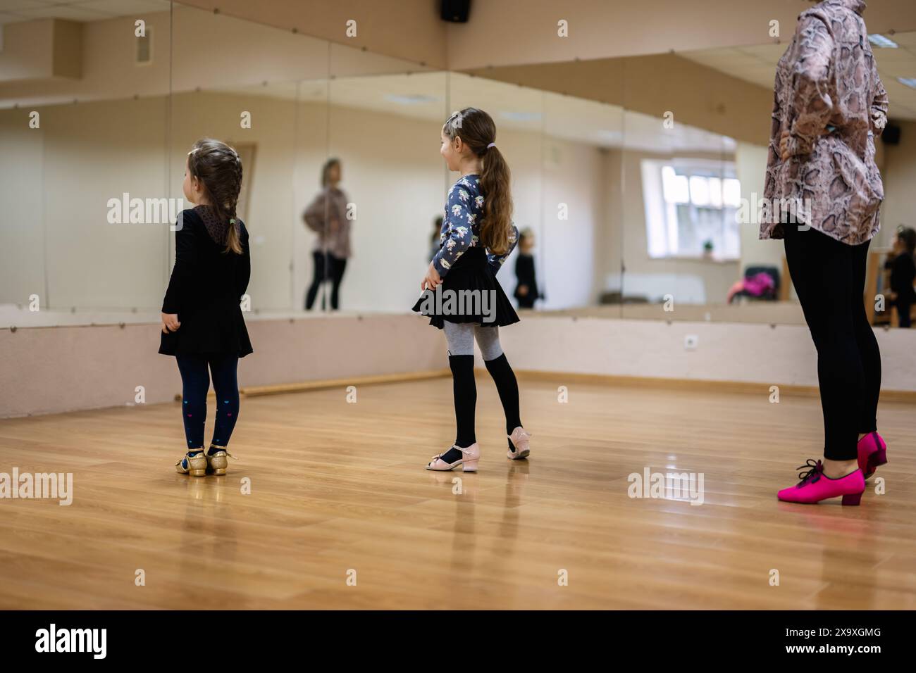 Deux jeunes filles dans un studio de danse, pratiquant avec leur instructeur. Ils sont habillés en tenue de danse, debout sur un plancher en bois avec des miroirs réfléchissent Banque D'Images