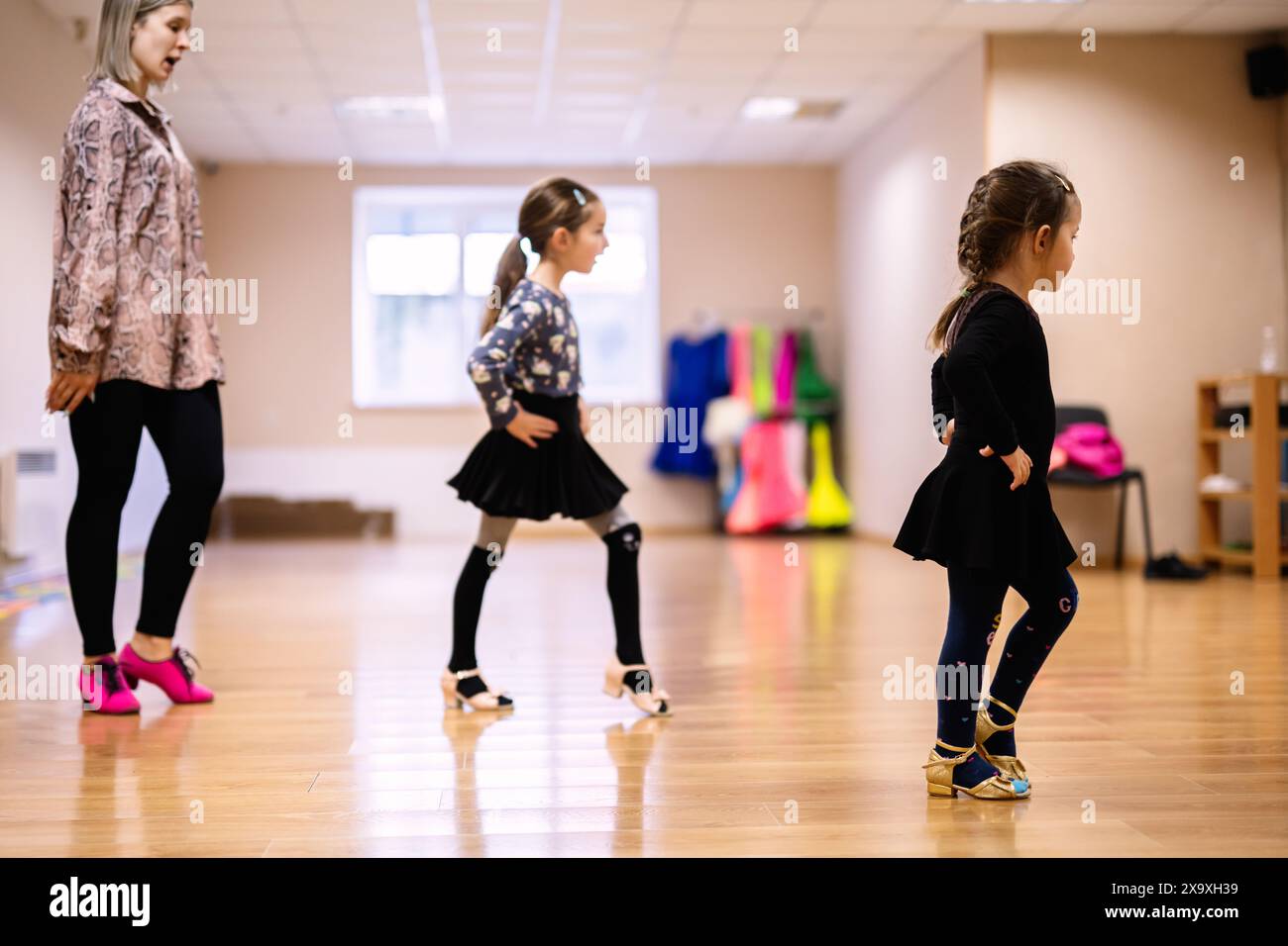 Deux jeunes filles pratiquant des pas de danse sous la direction d'un instructeur dans une salle de classe de danse. Concentrez-vous sur le mouvement, l'apprentissage et la concentration. Banque D'Images