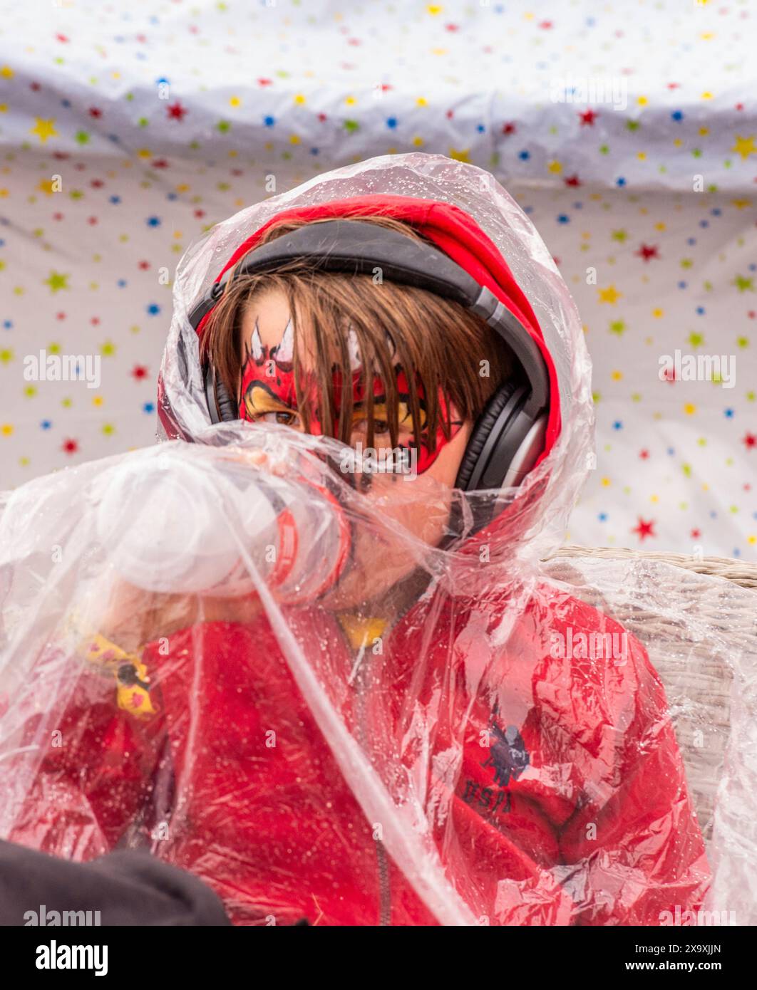 Un jeune festivalier au visage peint et à la tenue rouge se protège de la pluie battante au Latitude Festival à Henham Park dans le Suffolk. Banque D'Images