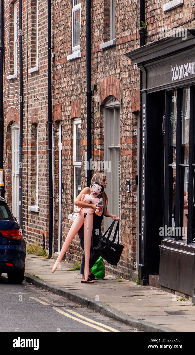Une dame porte une fausse poupée sexuelle à l'extérieur d'une maison en briques rouges à York alors qu'elle entre dans une propriété. Banque D'Images