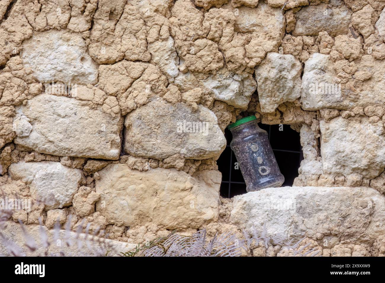 Un pot en verre plein de noix et de rondelles dans un petit trou dans un ancien mur d'adobe, dans une ferme dans les montagnes andines orientales du centre de la Colombie. Banque D'Images