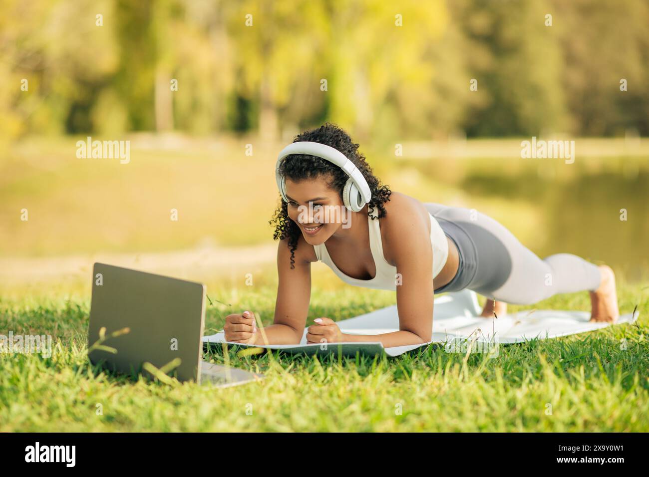 Dame s'exerçant à l'extérieur sur le tapis de yoga dans Sunny Park matin Banque D'Images
