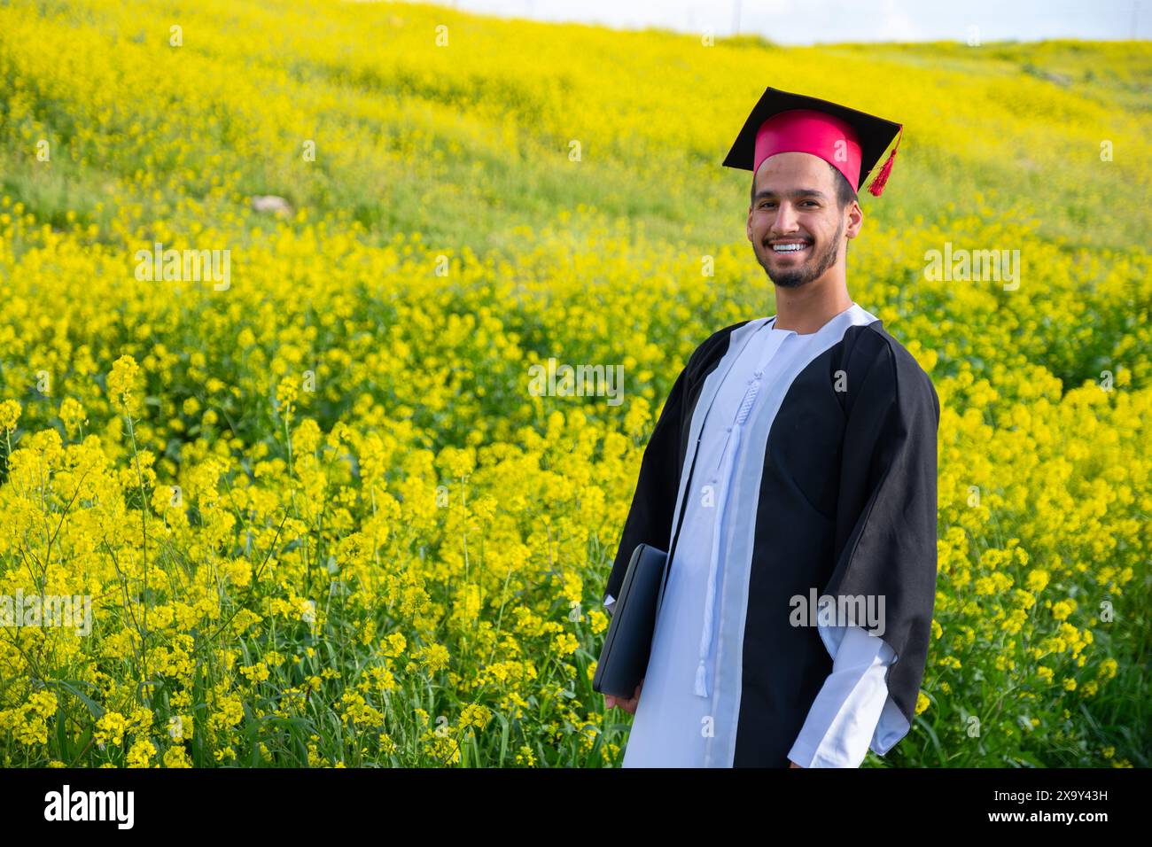 Jeune homme arabe célébrant sa remise des diplômes avec des roses autour et un look naturel Banque D'Images
