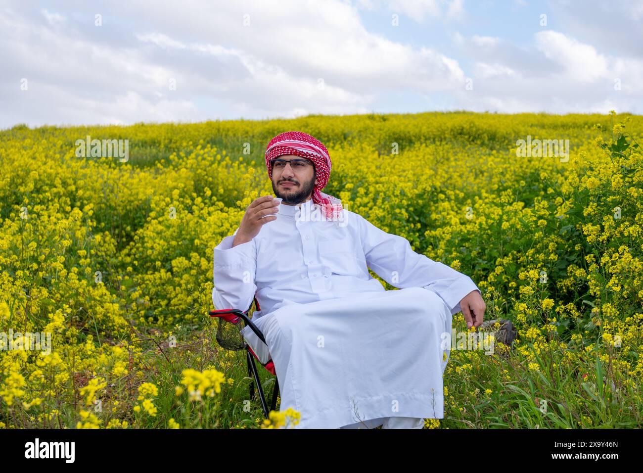Un peuple arabe profite d'un pique-nique printanier dans une prairie près d'Abu Dhabi. Assis sur des chaises, ils savourent des tasses de café sous un ciel bleu avec des nuages éparpillés Banque D'Images