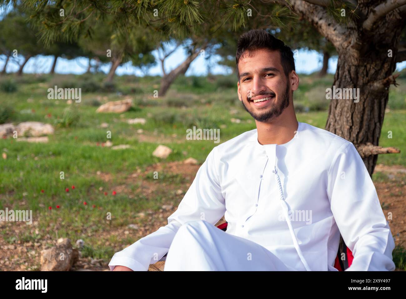 Un individu arabe est assis dans un champ doré de roses au lever du soleil, les bras levés dans la positivité. L'air frais du printemps et le ciel vibrant symbolisent la santé et fr Banque D'Images