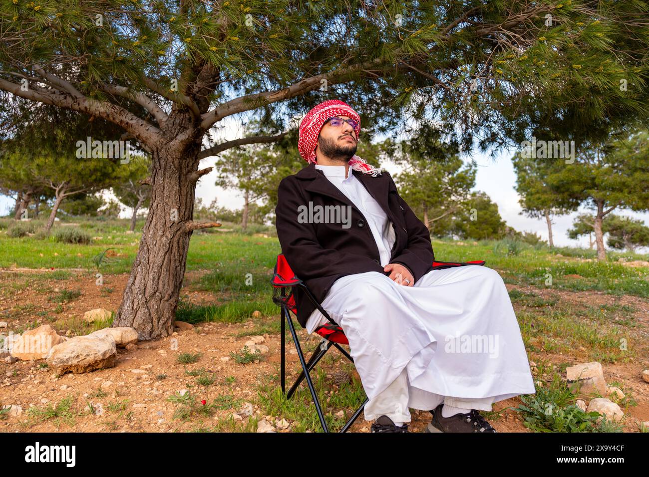 Un individu arabe est assis dans un champ doré de roses au lever du soleil, les bras levés dans la positivité. L'air frais du printemps et le ciel vibrant symbolisent la santé et fr Banque D'Images