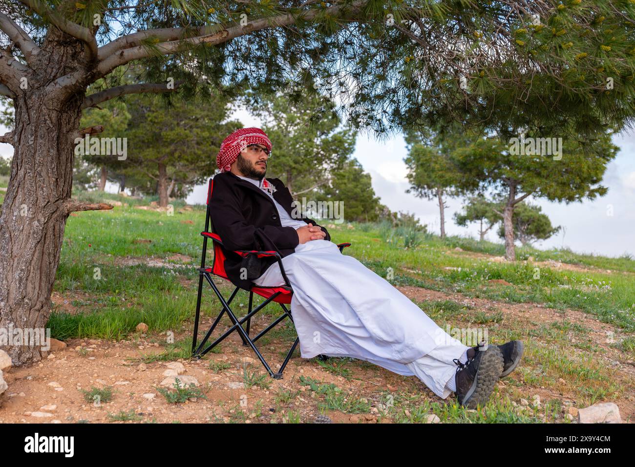 Un peuple arabe profite d'un pique-nique printanier dans une prairie près d'Abu Dhabi. Assis sur des chaises, ils savourent des tasses de café sous un ciel bleu avec des nuages éparpillés Banque D'Images