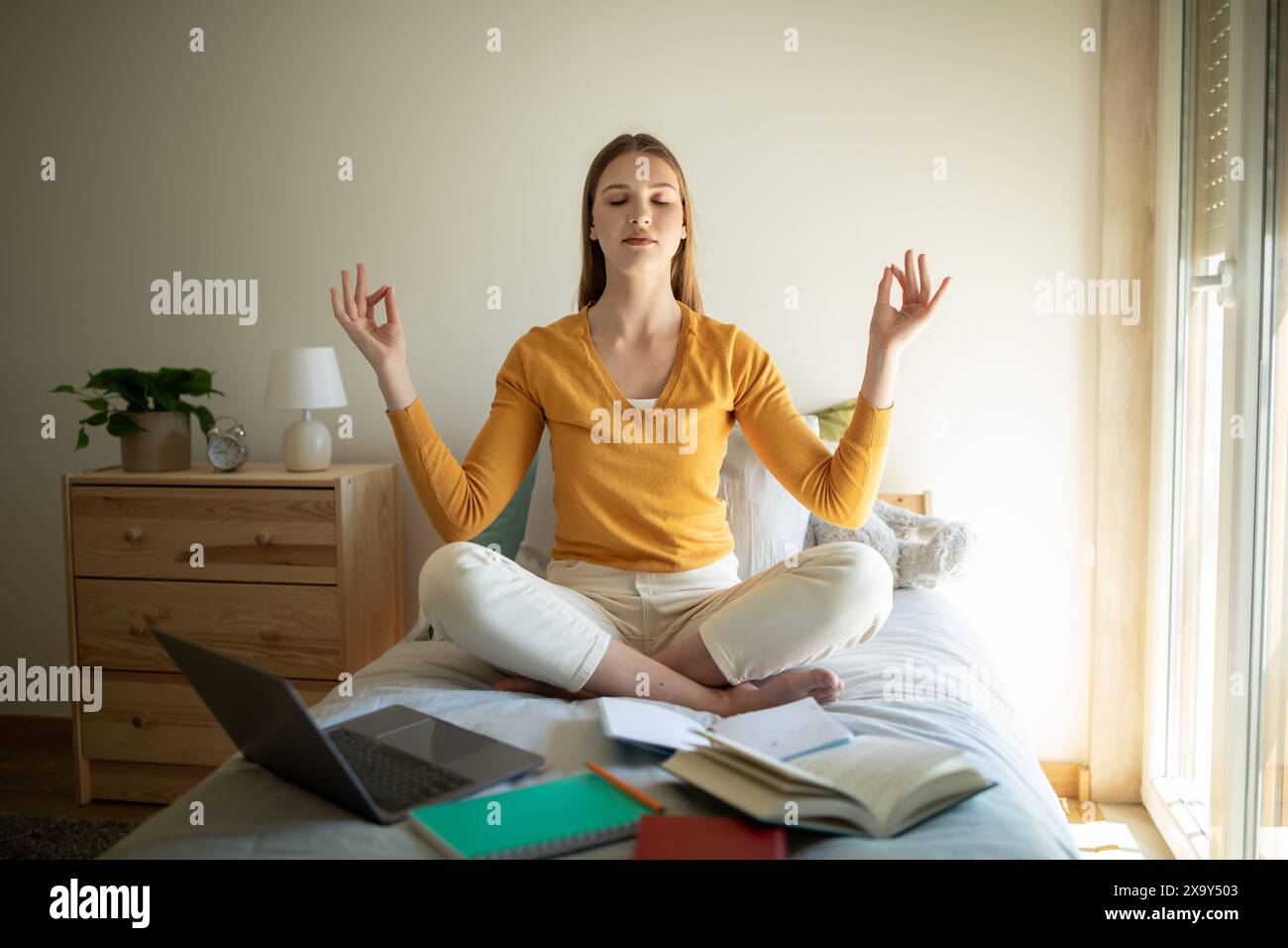 Fille méditant sur le lit entourée de matériel d'étude pendant la journée Banque D'Images