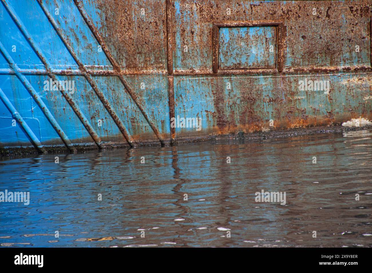 Structure rouillée sur une coque bleue abandonnée dans un port Banque D'Images