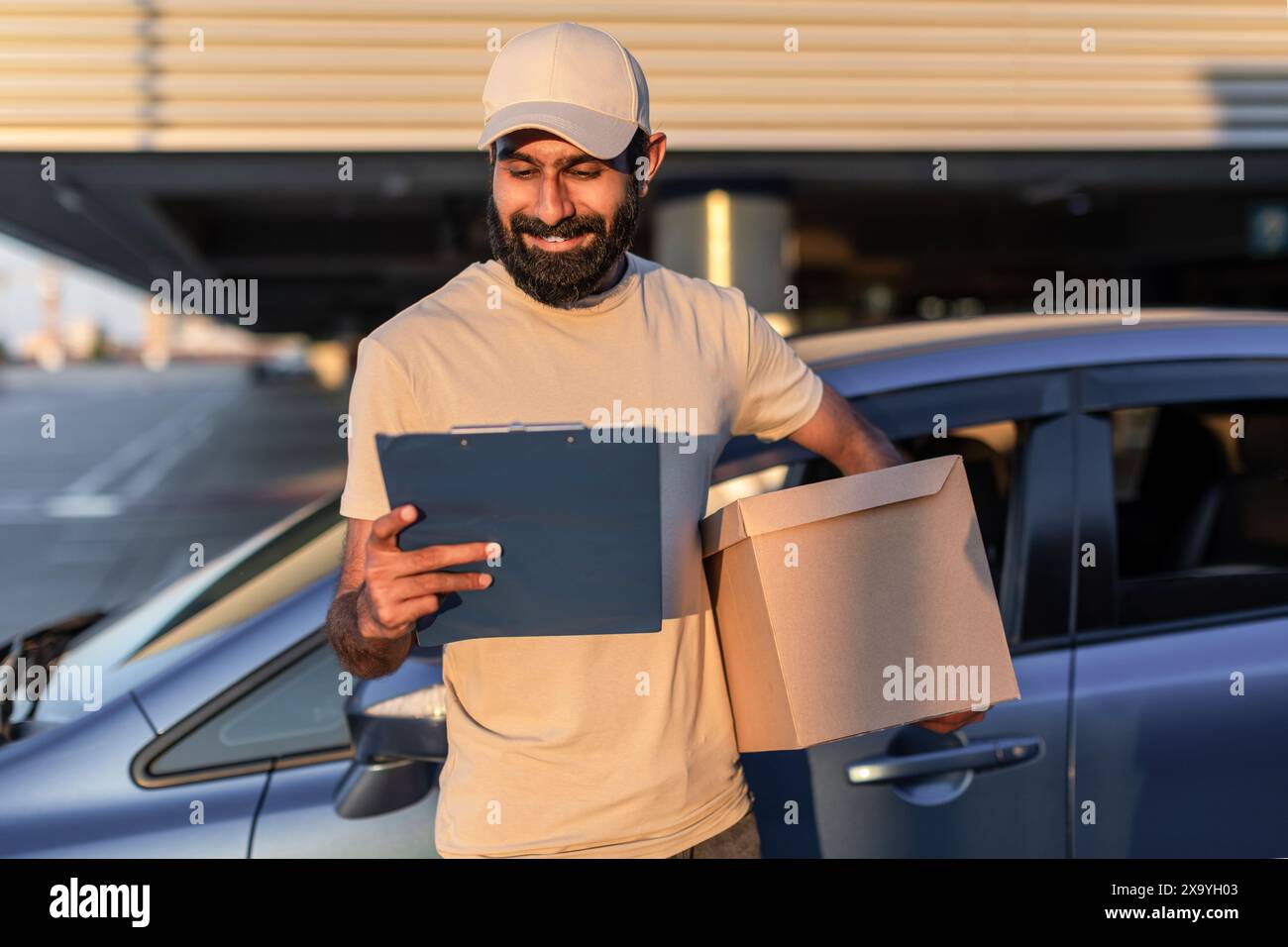 Boîte et presse-papiers du chauffeur de livraison souriante dans le parking Banque D'Images
